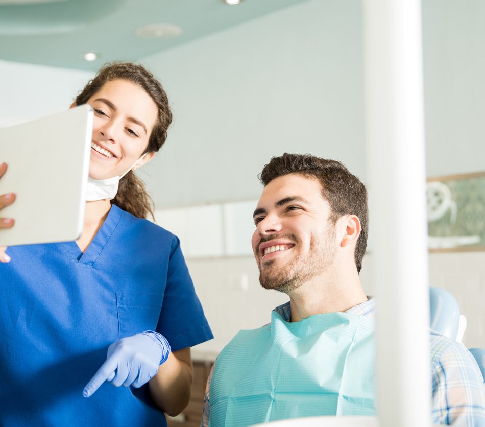 Smiling dentist and male patient looking at digital tablet during treatment in dental clinic